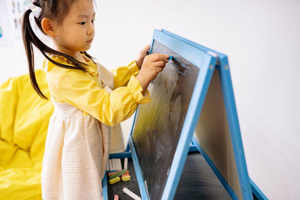 A young girl drawing on an easel in a bright classroom