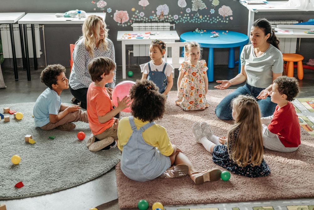 A teacher and a group of children playing together on a classroom floor