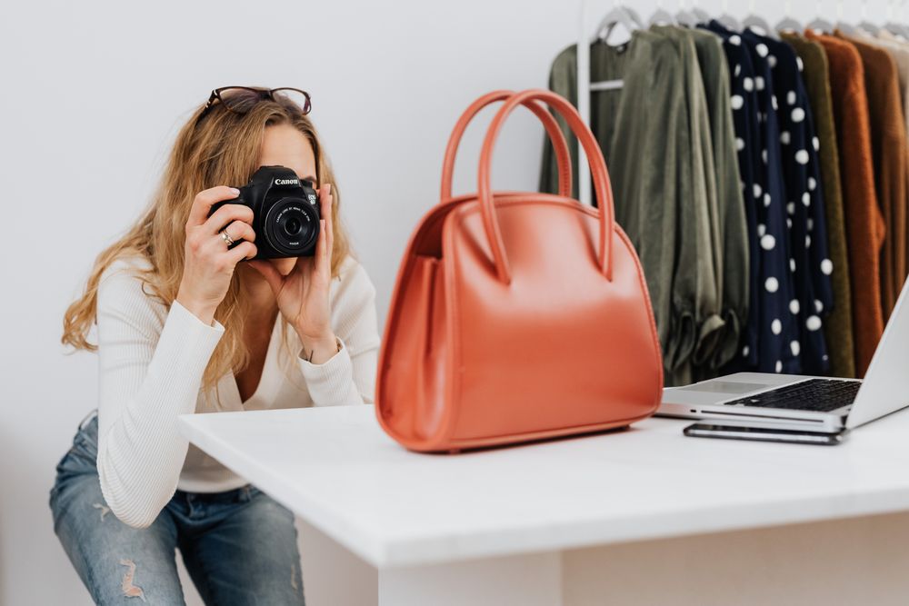 A photographer capturing a red handbag on a white table in a small product studio