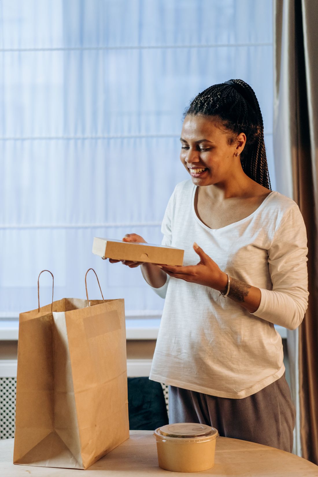 A woman unpacking a small parcel next to a paper bag in a bright room