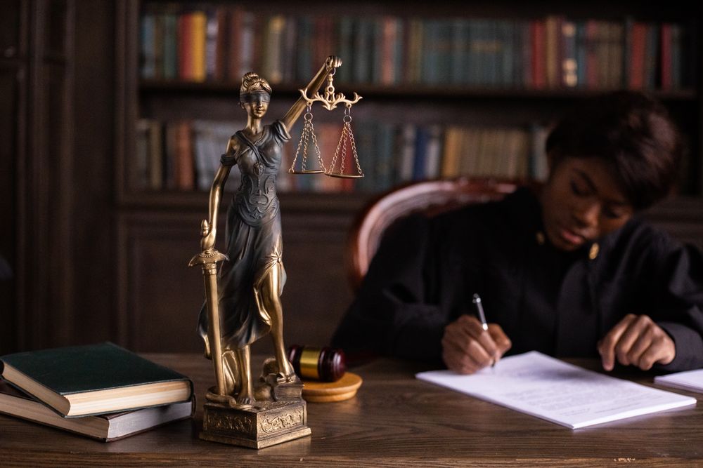 A lady justice statue on a desk while a lawyer takes notes