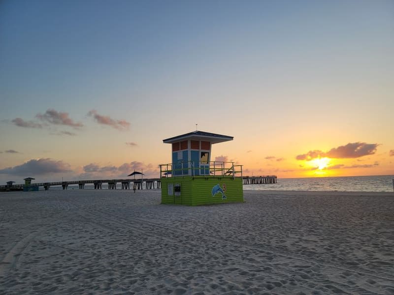 Lifeguard tower on the beach at sunrise with a pier in the distance
